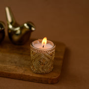 Decorative gold beaded candle holder with lit candle on wooden tray, brown background